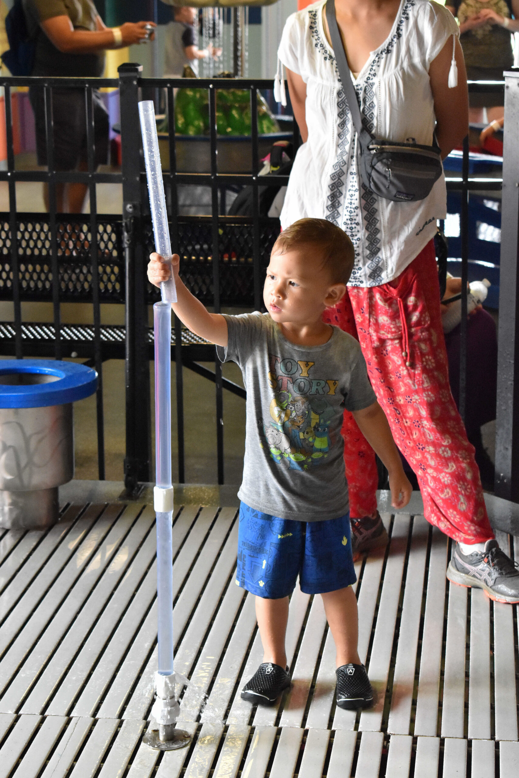 a young boy playing in water exhibit, holding a water tube